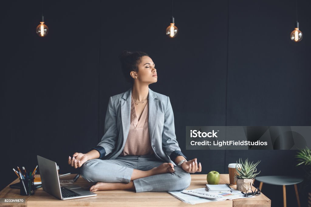 femme d’affaires afro-américain assis en lotus pose sur la table alors qu’il méditait dans le Bureau - Photo de Travailler libre de droits