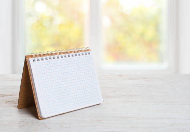 Notepad or calender on wooden table over blurred window background