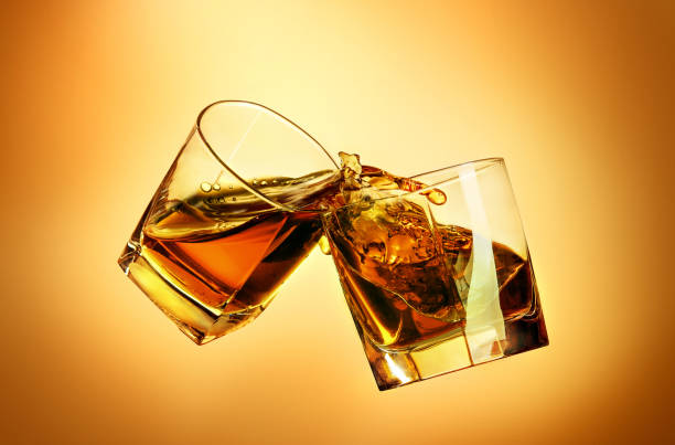 istock Two whiskey glasses clinking together on brown 823407574