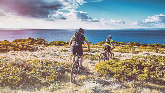 Couple on mountain bikes cycling on a dirt road along coastline.