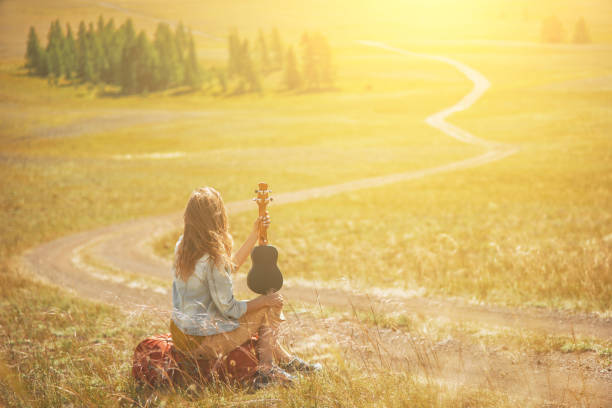 Young red hair woman play ukulele on the hill's summit. Mountain road landscape. stock photo