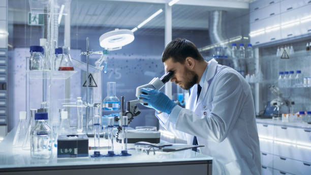 research scientist looks into microscope. he's conducts experiments in modern laboratory. - scientist research test tube lab coat imagens e fotografias de stock