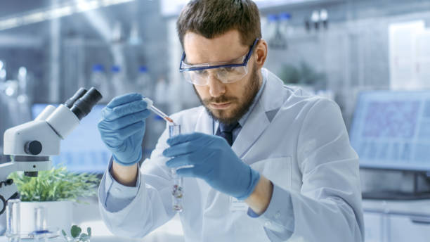 in a modern laboratory biologist conducts experiments by synthesising compounds with use of dropper and plant in a test tube. - smiling research science and technology clothing imagens e fotografias de stock