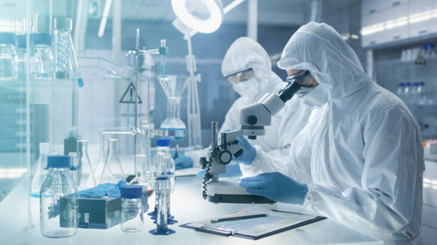 istock In a Secure High Level Laboratory Scientists in a Coverall Conducting a Research. Chemist Adjusts Samples in a  Petri Dish with Pincers and then Examines Them Under Microscope and His Colleague Writes Down Results. 823447782