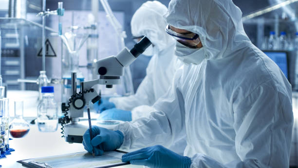 istock In a Secure High Level Laboratory Scientists in a Coverall Conducting a Research. Chemist with His Colleague Writes Down Experiment Results. 823447822