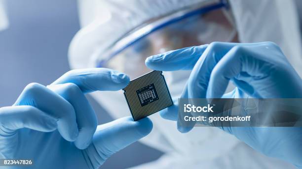 In Ultra Modern Electronic Manufacturing Factory Design Engineer In Sterile Coverall Holds Microchip With Gloves And Examines - Fotografie stock e altre immagini di Chip del computer