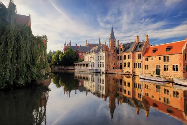 Historical centre of Bruges  in the evening sunlight. Bruges river view. Old Bruges buildings reflecting in water canal. Vibrant blue sky over Belgium landmarks.