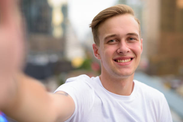 portret van jonge knappe tiener vlogging en nemen selfie met mobiele telefoon tegen uitzicht over de stad in bangkok thailand - alleen één tienerjongen stockfoto's en -beelden