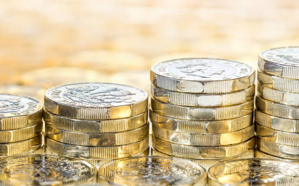 Ascending stacks of gold coins with coins background. Wrexham, UK - April 06, 2017: Ascending stacks of money. New shiny gold coins on a background of more coins. Blurred background. British pound coins. british currency stock pictures, royalty-free photos & images