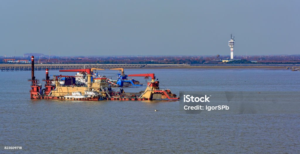 Cutter suction dredgers at work Cutter suction dredgers at work of land reclamation for new ports positioned on spuds as anchors and discharge dredged soil through a floating pipeline. Shanghai, China China - East Asia Stock Photo