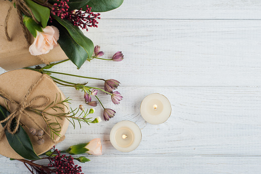 Gifts and flowers on wooden background. Top view, flat lay with lit candles and leaves