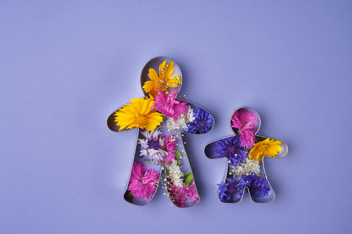Two iron figurines of dad and child on the blue flat with a lot of flowers inside. The mix of flowers on the blue flatness.