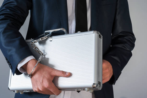 Man in elegant suit holding a suitcase tied with handcuffs to his hand stock photo