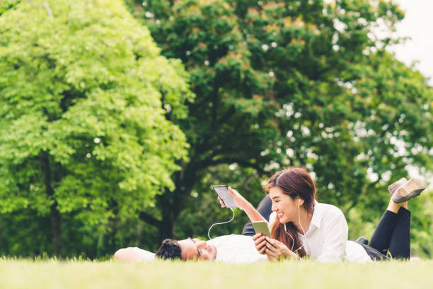 young asian lovely couple or college students listening to music together in the garden, with copy space. leisure activity, love relationship, wedding, or relaxing casual lifestyle concept - chinese ethnicity audio imagens e fotografias de stock