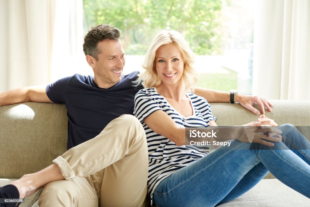 Relaxing together at home Full length shof a happy mature couple sitting on couch at home and relaxing togetherness. Domestic Life Stock Photo