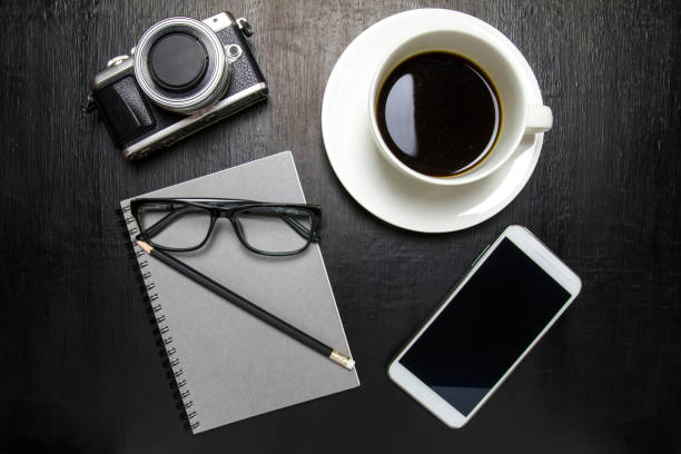 istock Top view of office desk workspace with coffee cup, notebook, camera, pencil ,mobile phone ,glasses on wooden background 823673010