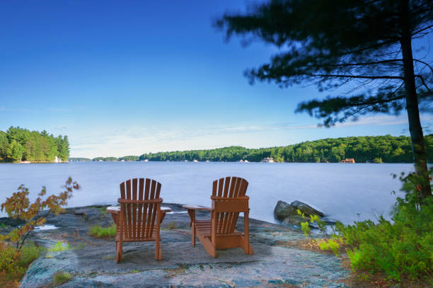 vita da cottage - sedie muskoka di fronte a un lago - adirondack chair foto e immagini stock