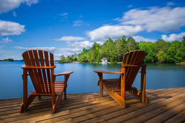 Muskoka chairs on a dock facing a lake stock photo