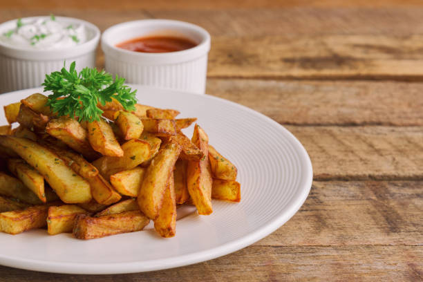 homemade french fries serve with ketchup and sour cream or mayonnaise. golden brown crispy french fries sprinkle with salt and oregano on white plate for snack or appetizer.french fries on wood table. - oregano freshness herb brown imagens e fotografias de stock
