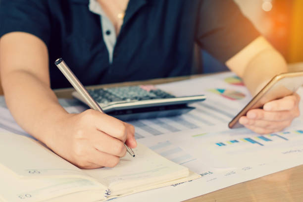 istock close up hand woman calculating about cost and using smartphone searching data in office. 823680084