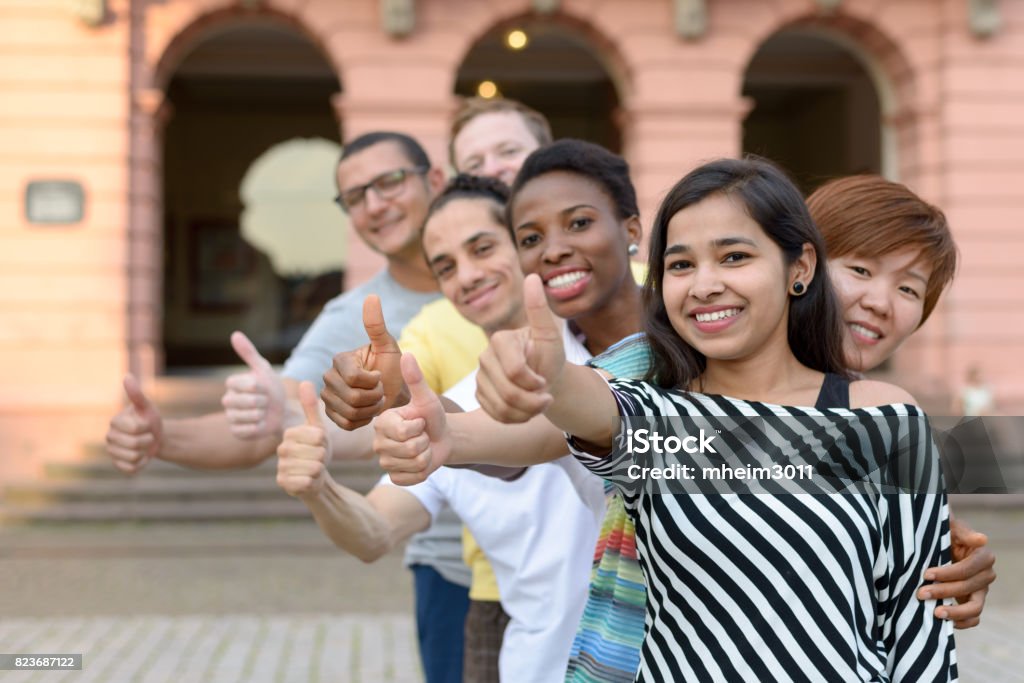Group of young people with thumbs up Smiling diverse group of young people in row giving thumbs up sign Group Of Objects Stock Photo