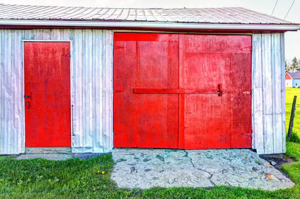 Red painted vintage shed with doors in summer landscape field in countryside
