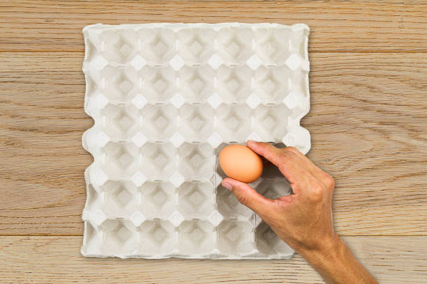 Man's hand picking up one last egg from paper tray on wooden background