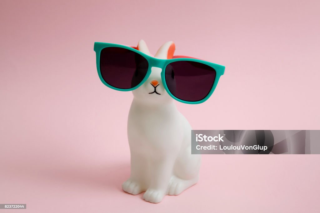 Sunglasses bunny a cute white plastic bunny wearing sunglasses on a pink background."nMinimal color still life photography Easter Stock Photo