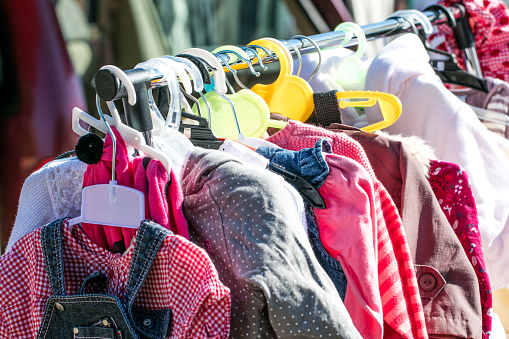 rack of beautiful second hand baby girl and children jackets and clothes displayed at outdoor garage sale for shopping, reusing, exchanging, recycling or donating