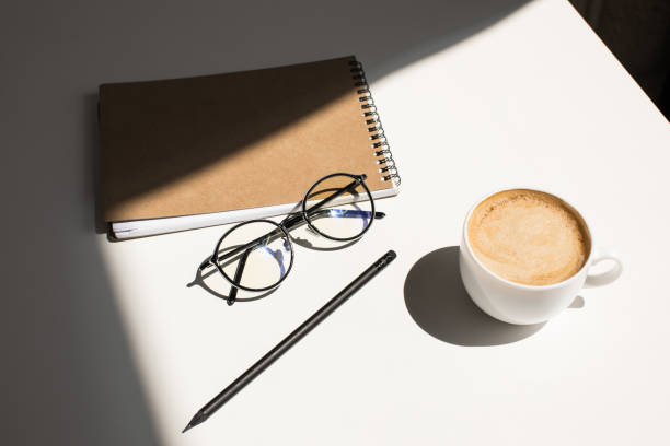 istock cup of coffee, eyeglasses and notepad on white tabletop with sunlight 823742230