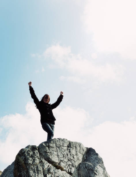 istock Successful young woman stands on high rock gesturing in triumph 823747272