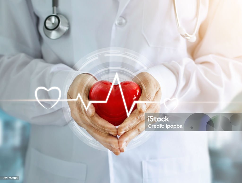 Doctor with stethoscope and red heart shape with icon heartbeat in hands on hospital background Heart Disease Stock Photo