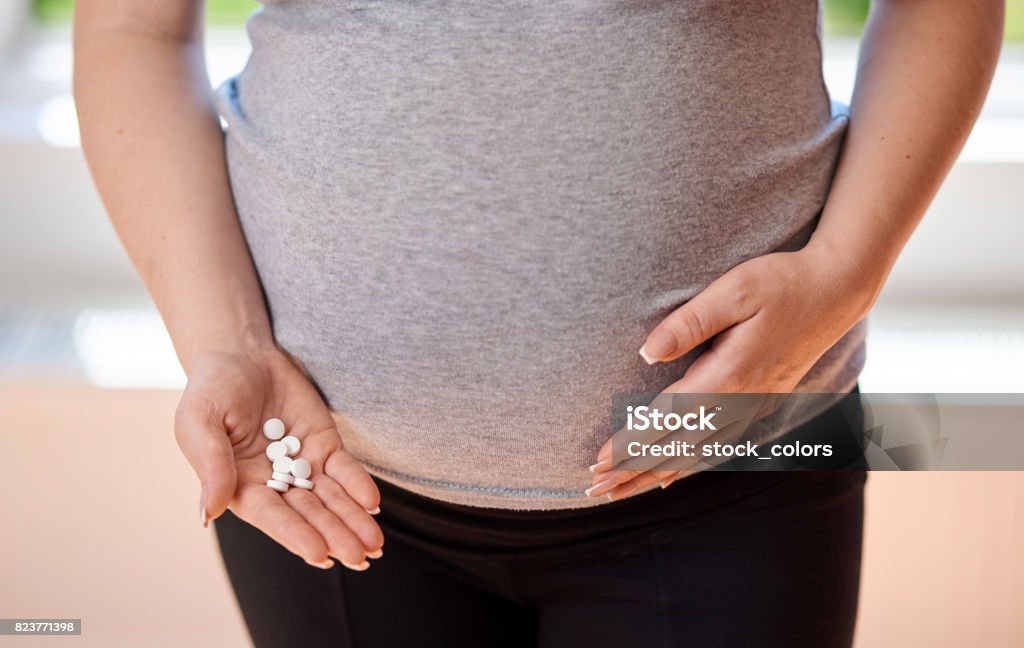 try to feel better unrecognizable pregnant mother holding white pills in her hand. Abdomen Stock Photo