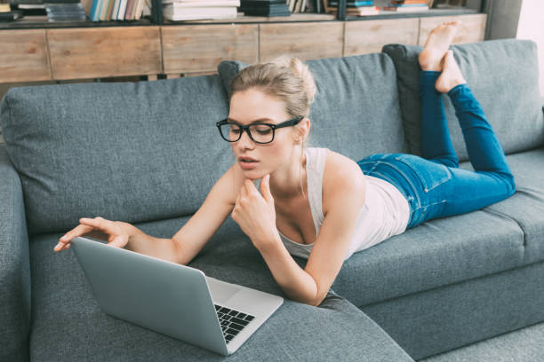 istock Young blonde woman using laptop on sofa in living room 823771904