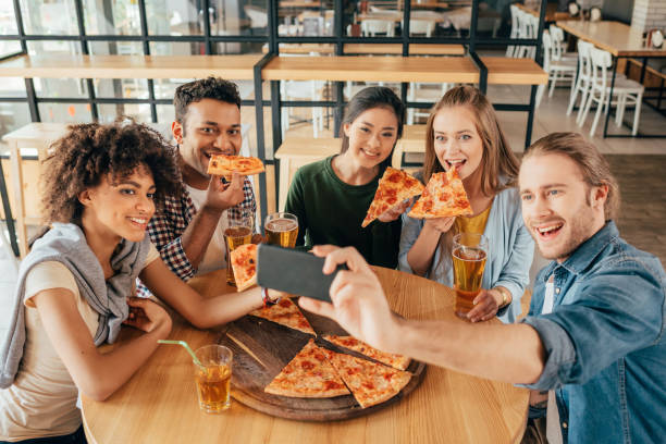 カフェでピザを抱えている多民族の友人と selfie を取る若い男 - pizza pizzeria friendship people ストックフォトと画像