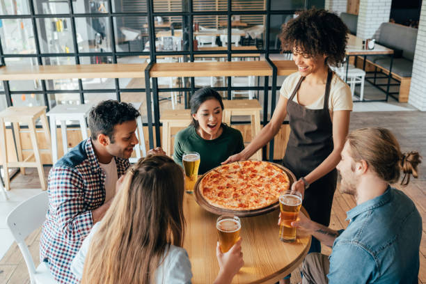 serveuse femme afro-américaine, apportant la pizza pour les clients en café - pizza pizzeria restaurant waiter photos et images de collection