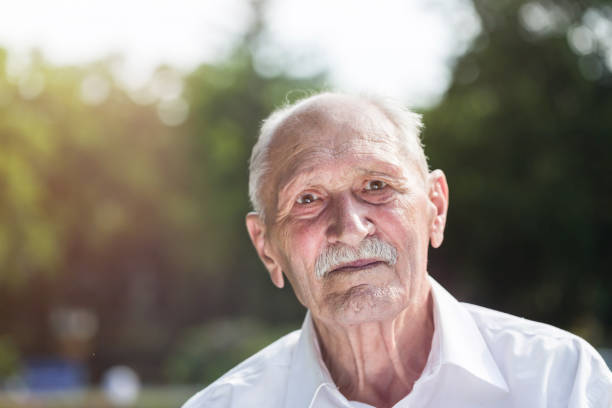 istock old man portrait, sitting on a bench in a park in summer 823807194