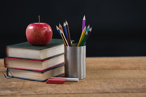 Close-up of school supplies and books stack with red apple on top