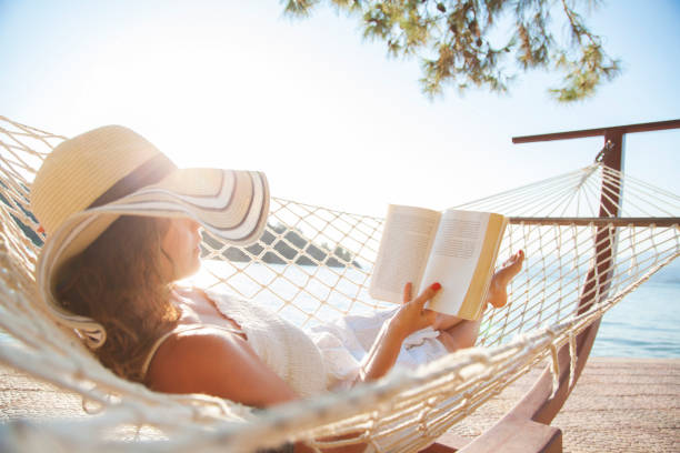 donna su un'amaca con libro in vacanza - summer vacations women hammock foto e immagini stock