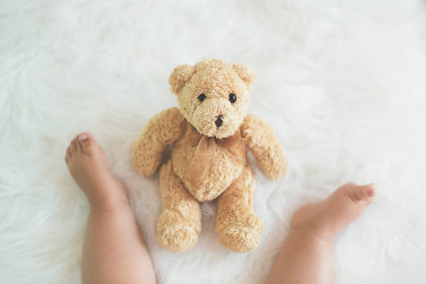 Teddy bear in front of baby, sitting on fluffy blanket - low section