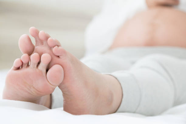 les femmes enceintes du sud-est asiatiques avec gonflement des pieds, douleur pied et couché sur le lit dans la chambre. pieds enflés et le concept de toxicité ou d’intoxication foetale - intoxication photos et images de collection