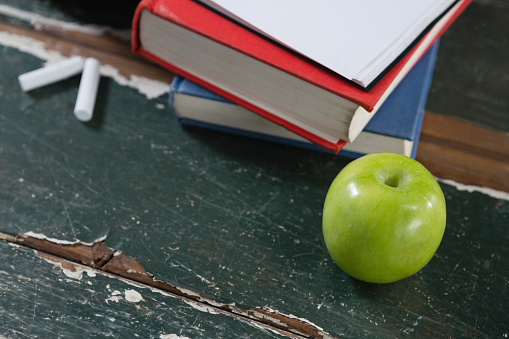 Close-up of books, green apple and chalk on wooden table