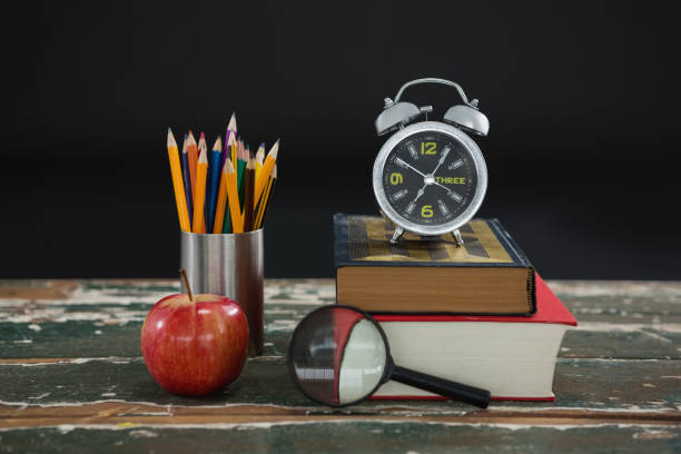 istock Alarm clock on stack of books with pen holder, apple, and magnifying glass 823847024
