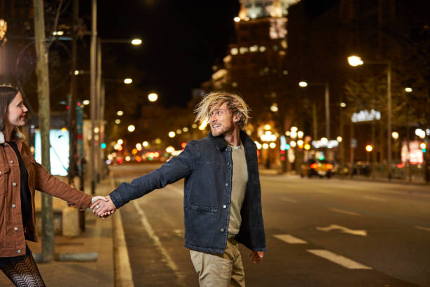 Couple holding hands while crossing road at night