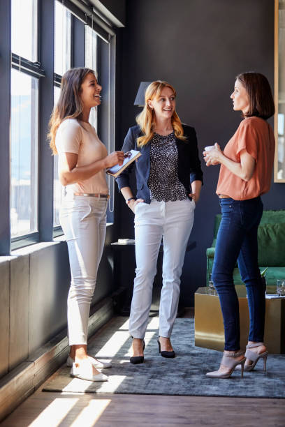 imprenditrici che discutono per finestra in ufficio - three people group of people standing business person foto e immagini stock