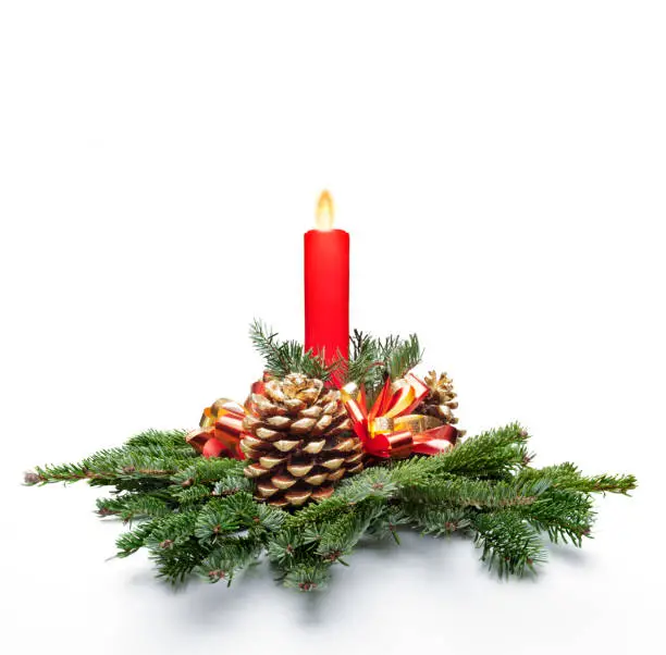Christmas centerpiece decoration with a red color candle lit and fir tree leaves. White background.