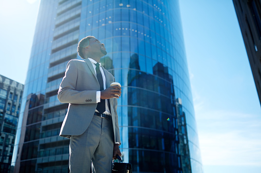 Businessman with drink looking at modern skyscraper