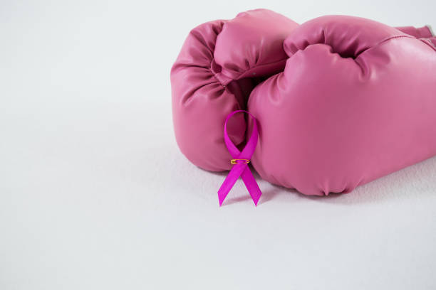 gros plan du ruban rose de sensibilisation au cancer du sein avec paire de gants de boxe - elementary age focus on foreground indoors studio shot photos et images de collection