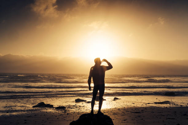 istock Man stood drinking water after a run along the beach. 823932284