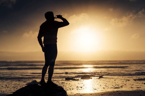istock Man stood drinking water after a run along the beach. 823932296